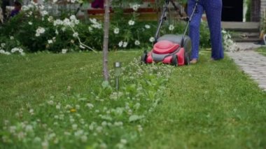 Bahçesinde çim biçen kadın elektrikli çim biçme makinesiyle.