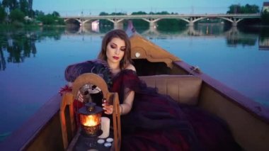 Burgundy uzun elbiseli zarif bir kadın dekoratif bir fenere dokunuyor ve akşamları nehrin arka planındaki gondolda gülümsüyor. Karnaval