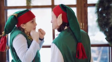 Uzun kulaklı komik elfler tatil beklentisiyle pencereden dışarı bakıyor ve yılbaşı süslemelerinin arka planında birlikte dans ediyorlar. Arka plan bulanık. Yakın plan.