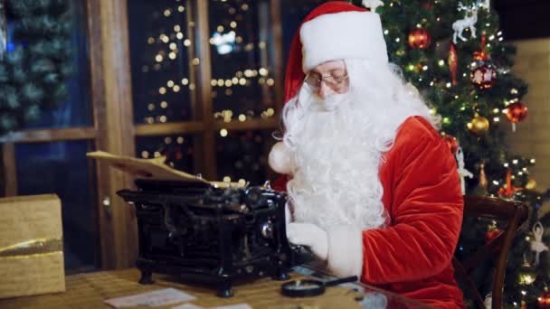 전통적 의상을 산타클로스는 타자기에 편지를 확대경을 사용하여 사람의 주소가 봉투를 — 비디오