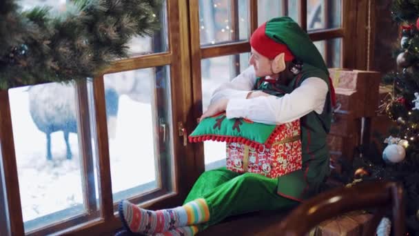 Elfo Terno Verde Sentado Peitoril Janela Com Presente Mão Travesseiro — Vídeo de Stock