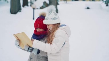 Şirin çocuklar ellerinde büyük bir zarf tutuyorlar ve kışın sokağın ortasında üzerinde adresi okuyorlar. Chidren mektup vermek için bir ev adresi arıyor. Ağır çekim. Bulanık arkaplan