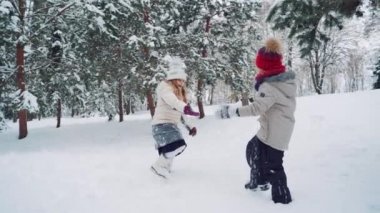 Çocuklar bahçede el ele tutuşuyor ve kışın ağaçların arka planında karlı bir tepede birlikte koşuyorlar. Yavaş çekim