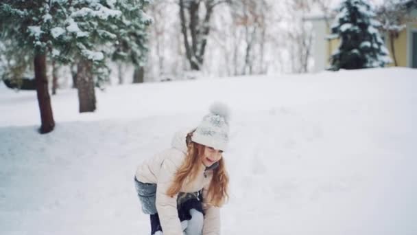 一个长头发的微笑的女孩在冬天的降雪时 把雪球扔在院子里的街上 慢动作 — 图库视频影像