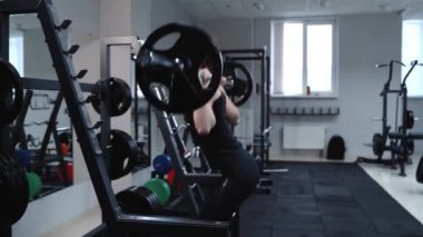 Siyah spor giyimli güçlü bir kadın spor salonunda halterle egzersiz yapıyor. Çömelme.