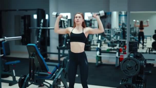 一个年轻的女人手里拿着铁制的哑铃 在运动器材的背景下提起哑铃 抽打体育馆里的二头肌 — 图库视频影像