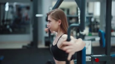Güçlü kolları olan güzel bir kız bir fitness kulübündeki göğüs kaslarını güçlendirmek için simülatör üzerinde egzersiz yapıyor. Yakın plan. Bulanık Arkaplan