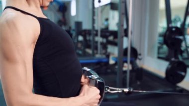 Siyah bluzlu bir kadın, spor malzemelerinin arka planına karşı bir fitness kulübünde basın ve pazıları pompalamak için egzersiz yapıyor. Yakın plan.