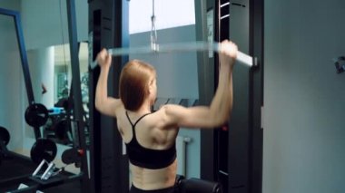 Siyah bluzlu güçlü bir kadın spor salonunda dikey çekiş yapıyor. Yakın plan.