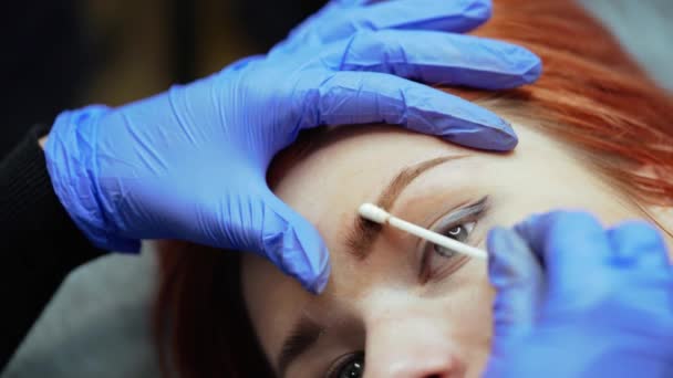 美容师完成纹身眉毛的过程 并用棉签在美容院里擦拭客户的眉毛 后续行动 — 图库视频影像