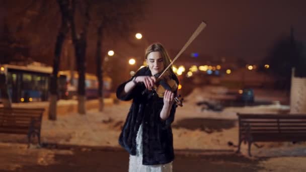一个漂亮的女孩正在市中心的马路附近的公共交通中弹奏小提琴 模糊的背景 — 图库视频影像