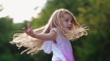 Güzel çocuk doğada çimlerde dönüyor. Yavaş çekim uzun saçlı tatlı kız yeşil çayırda eğleniyor ve doğanın tadını çıkarıyor.