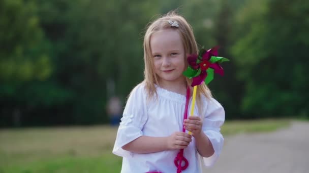 夏天的时候 小女孩手里拿着风车 快乐地微笑着的小女孩站在公园里手握飞轮 — 图库视频影像