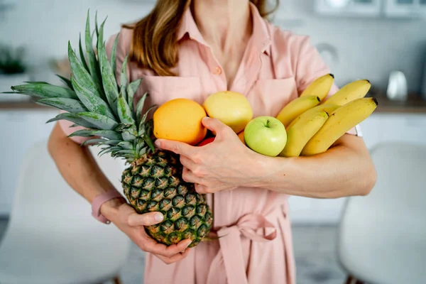 現代のキッチンの背景に果物を持つ若い女性 健康的な食べ物と食事の概念 手にパイナップルと柑橘類 切り取られた写真 — ストック写真