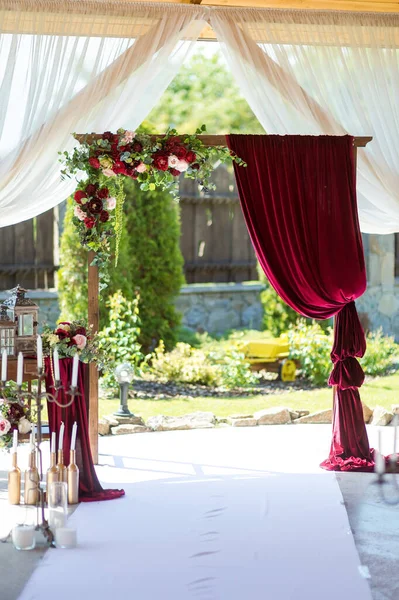 Wedding arch in restaurant. Dark red flowers and burgundy curtains. Ceremony decorations.