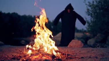 Keşiş kamp ateşinde dua ediyor. Cüppeli bir adam ateşin etrafında gösteri yapar.