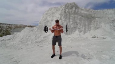 Adam dağda eğitim görüyor. Sporcunun antrenman kıyafetleri içinde, halterle dağın tepesinde dikilirken.