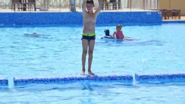 幸せな少年はプールに飛び込む アクティブなティーン男の子ジャンプへ屋外プール — ストック動画