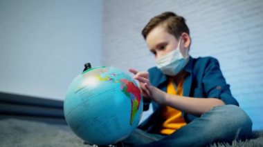 Dünyaya bakan bir çocuk virüsün tüm dünyaya yayıldığını öğreniyor. Tıbbi maske takan çocuk. COVID-19 salgını konsepti.
