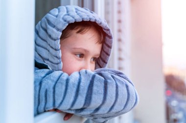 Çocuk ayağa kalktı ve pencereden dışarı baktı. Evde kal ve karantina konseptini uygula. Üzüntü. Salgın sırasında izolasyon.