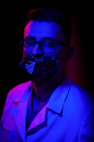 Doctor wears mask. Black background with blue - red light. Doctor in glasses closed mouth with medical mask. Close up shot