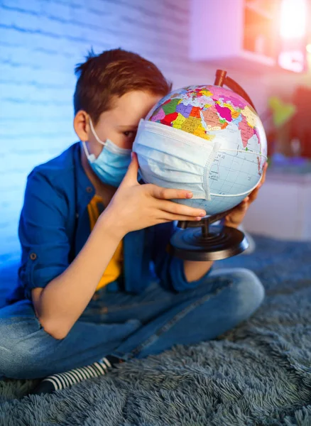 A child in a medical mask holds a globe. Little boy heals the planet. Concept of air and environment pollution.