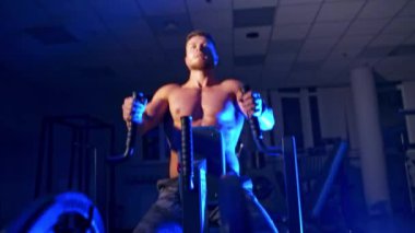 Spor salonunda egzersiz yapan yakışıklı bir adam. Kas yığını atletik vücut geliştirici adam mavi arka planda spor salonunda sıkı çalışıyor.