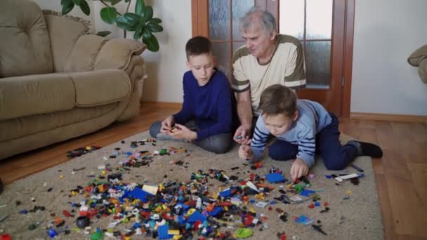 少年たちは家でレゴのおもちゃを遊んでいる 面白いかわいい子供たち遊びLegoとともに家で祖父 — ストック動画