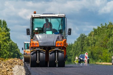 Yol silindiri yeni asfaltı dümdüz ediyor. Ağır titreşim silindiri asfalt döşeyip yol tamiri yapıyor. Seçici odak.