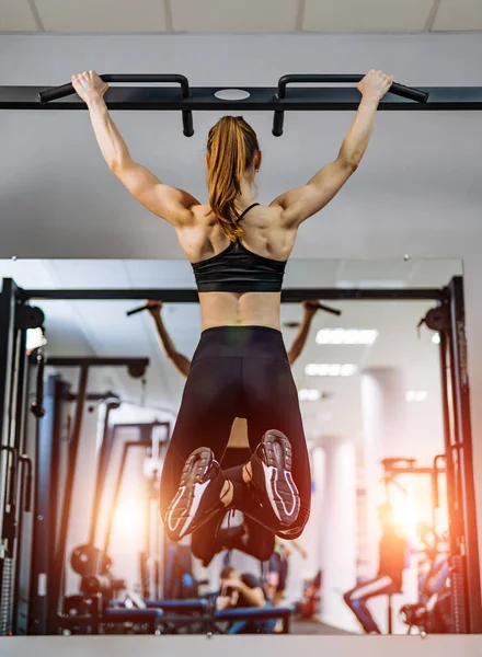 The sport girl pulls up on the horizontal bar in the gym. Art photo. Doing twisting on bar. Back photo