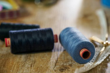 Ahşap masa arkasında siyah ve mavi iplikli bobinler. Dikiş konsepti.