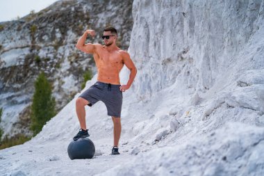 Açık havada çıplak poz veren güçlü bir vücut geliştirici. Taş ocağında fotoşop. Açık hava sporları konsepti. Ön manzara. Formda poz vermek. Beyaz manzara
