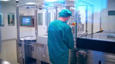 Eczacılık işçisi ilaç kullanıyor. İlaç endüstrisinde koruyucu giysi işçisi steril çalışma koşullarında tablet üretimi yapıyor.
