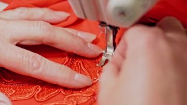 Kadın dikiş makinesine elbise dikiyor. Kadın elleri dikiş makinesiyle kumaşa desen çiziyor.