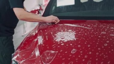 Makina özellikle film yapıştırıyor. Araba ambalajlama uzmanları hava kabarcıklarını temizlemek için filmi düzeltiyorlar