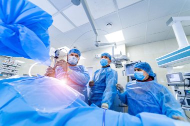 Ameliyathane ve ameliyat devam ediyor. Tıbbi ekip, parlak modern ameliyathanede cerrahi operasyon gerçekleştiriyor.