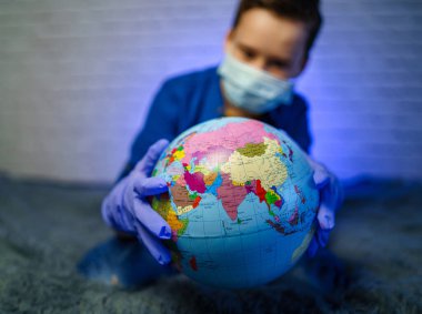Tıbbi maskeli bir çocuğun elinde bir dünya var. Küçük çocuk gezegeni iyileştiriyor. Hava ve çevre kirliliği kavramı.