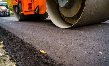 Asfalt kaldırımda ağır titreşimli silindir çalışıyor. Yol tamiri. Seçici odaklanma, kırpılmış fotoğraf. Yeni asfalt.