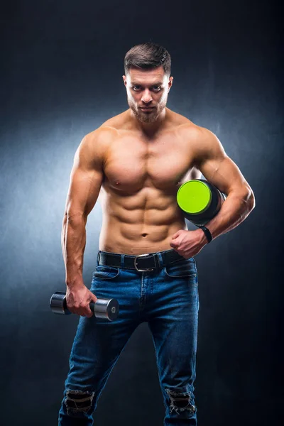男性アスリートボディビルダーは 手にスポーツ栄養とダンベルの瓶を保持しています — ストック写真