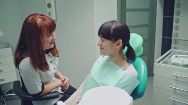 Diş sağlığı kliniği. Resepsiyon, hastanın muayenesi. Diş bakımı. Diş muayenehanesindeki kadın dişçi kız hastayla konuşuyor.