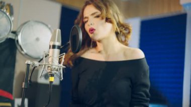 Modern bir ses stüdyosunda siyah giyinmiş, şarkı söyleyen mutlu bir kadının portresi. Güzel bir şarkıcı ve müzik aletinin yan görüntüsü