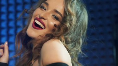 Parlak makyajlı, kameraya bakan ve mavi arka planda izole bir şekilde gülümseyen muhteşem bir kadın. Uzun dalgalı saçlı hoş bir şarkıcının portresi. Yakın plan.