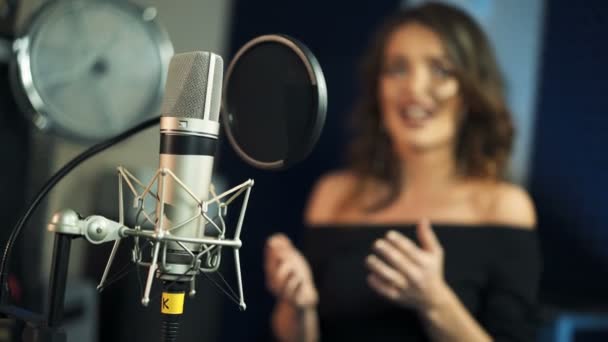 女性の歌のぼやけた背景にプロのコンデンサースタジオブラックマイク スタジオでの楽器と女性歌手 — ストック動画
