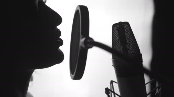 スタジオで曲を演奏するマイクの前でプロの歌手 女性の顔の歌の魅力的なプロフィールビュー 接近中だ 白黒ビデオ — ストック動画