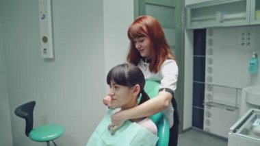 Dişçi gülümseyen hastayı stomatoloji dolabının arka planında diş tedavisi için hazırlıyor. Doktor ve genç kadın dişçi koltuğunda.