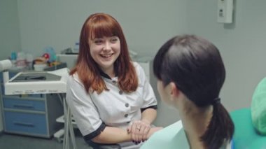 Stomatoloji kliniğinde bir hastayla konuşan mutlu dişçi kadın. Kadın hasta sandalyede oturuyor ve profesyonel dişçi doktorunu dinliyor.