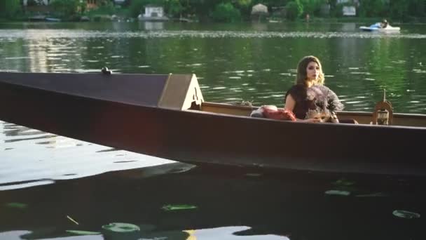 坐船的年轻漂亮的女人拿着羽毛 在河床上展示她的肩膀 夏天飘浮着一头长长的黑发的性感女性 — 图库视频影像
