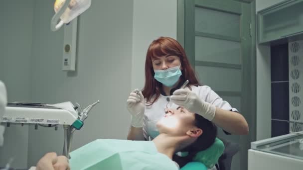 歯科機器の背景にあるクリニックの女性患者に歯を治療する美しい歯科医 仕事中の女性専門医の胃科医 — ストック動画