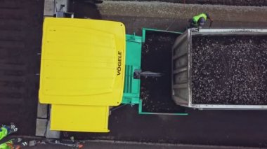 Bitumen ve molozlarla dolu büyük bir kamyon, yeni asfalt şeridin arka planındaki kaldırıma yanaşıyor ve etrafta birkaç kişi var. Yol tamiri. Hava görünümü.