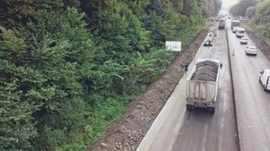 Bitumen 'lı bir kamyon, şehrin yakınlarındaki yol onarım çalışmalarının arka planına inen bir ormanın yakınındaki bir patikaya doğru yavaşça ilerliyor. Hava görünümü.